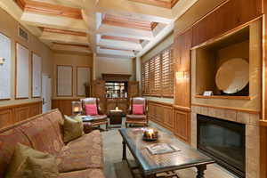 Living area with coffered ceiling, a wainscoted wall, a tiled fireplace, crown molding, and light carpet