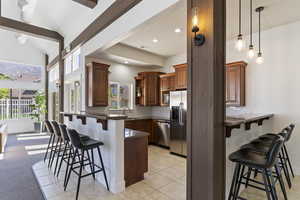 Kitchen featuring a breakfast bar, a peninsula, wood finish cabinets, dark stone countertops, and lofted ceiling with beams