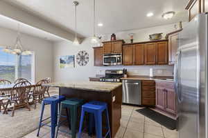 Kitchen featuring stainless steel appliances, pendant lighting, a kitchen breakfast bar, a kitchen island, and wood finish cabinetry