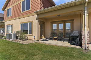 Rear view of house with stucco siding, a patio area, a lawn, and french doors