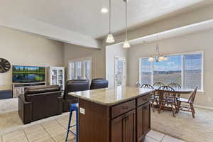 Kitchen with a kitchen breakfast bar, a center island, pendant lighting, light colored carpet, and light stone countertops