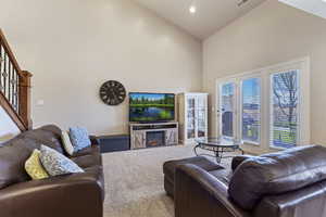 Carpeted living room with a glass covered fireplace, lofted ceiling, and recessed lighting