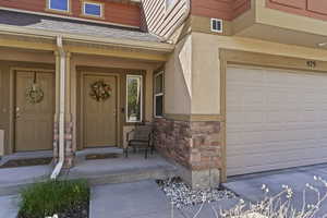 Entrance to property with covered porch, stone siding, stucco siding, and a shingled roof