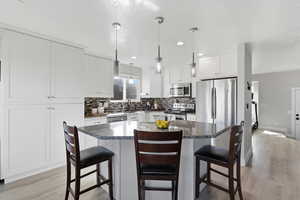 Kitchen with a kitchen breakfast bar, stainless steel appliances, white cabinetry, light wood-type flooring, and a textured ceiling