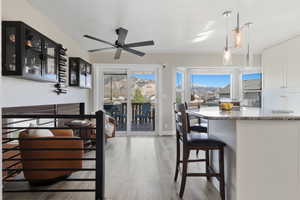 Kitchen with a kitchen bar, hanging light fixtures, light wood-style floors, a ceiling fan, and glass insert cabinets