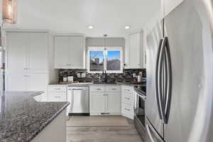 Kitchen featuring stainless steel appliances, dark stone counters, white cabinets, hanging light fixtures, and light wood-style flooring