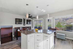Kitchen featuring white cabinets, ceiling fan, a kitchen island, dark wood-style floors, and dark stone countertops