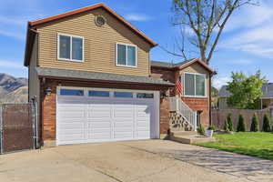View of front of property featuring concrete driveway, an attached garage, brick siding, a shingled roof, and a gate