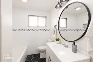 Full renovated bathroom featuring vanity, dark tile patterned flooring, and beautifully finished tile.