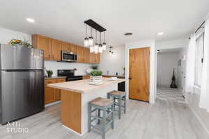Kitchen featuring stainless steel appliances, a breakfast bar area, a kitchen island, butcher block countertops, and decorative light fixtures