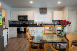 Kitchen featuring stainless steel appliances, white cabinetry, dark wood-type flooring, decorative backsplash, and recessed lighting