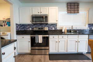 Kitchen with stainless steel appliances, white cabinetry, dark stone countertops, washer / dryer, and light wood-style floors
