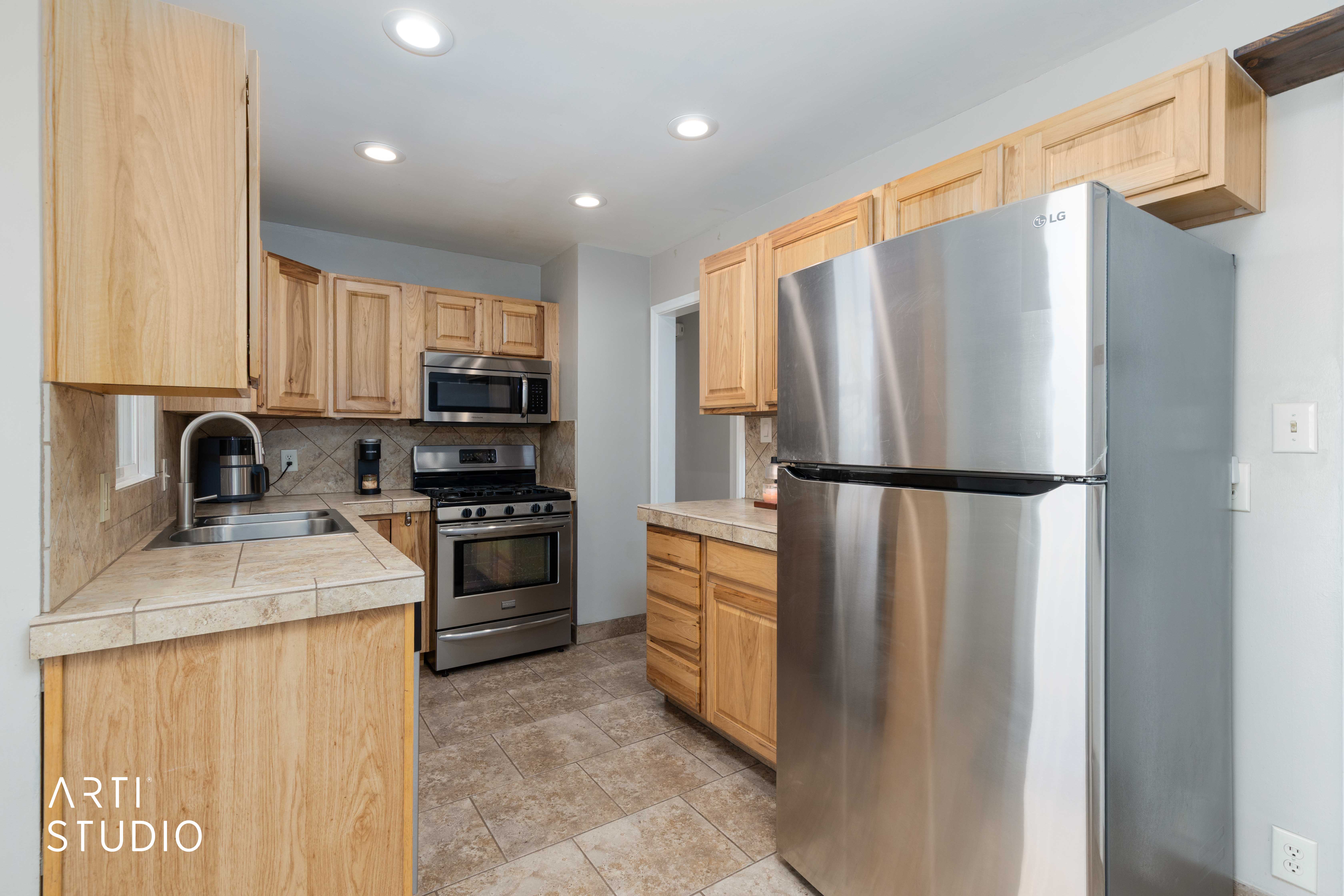 Kitchen featuring stainless steel appliances, backsplash, light wood finish cabinetry, recessed lighting, and tile countertops