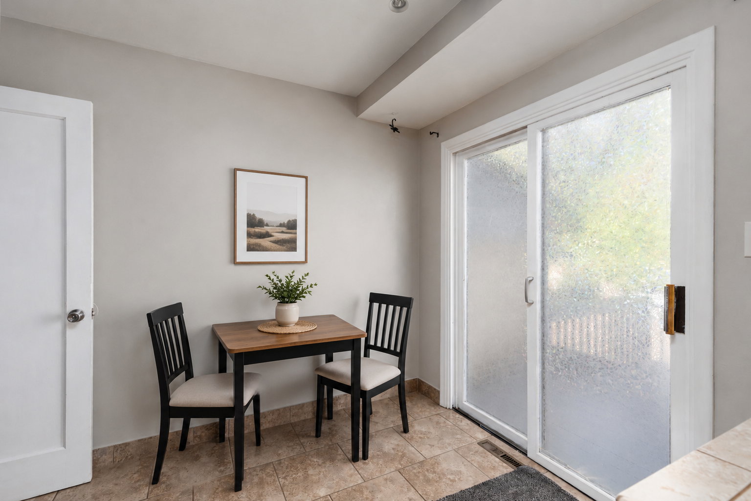 Sliding glass doors with frosted privacy panels, virtually staged with table, chairs, and wall art.