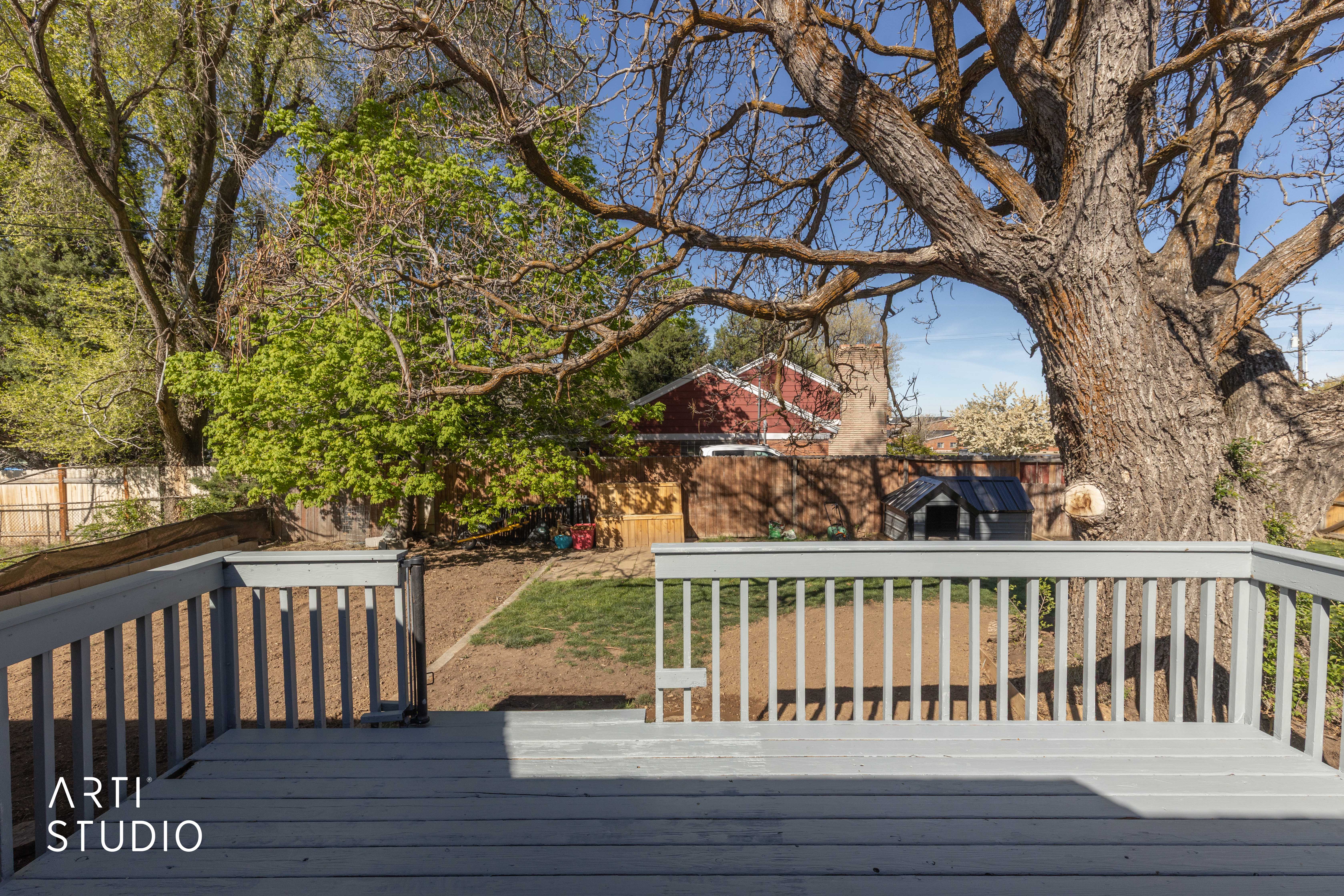 Wooden deck with a fenced backyard, and large shade tree.