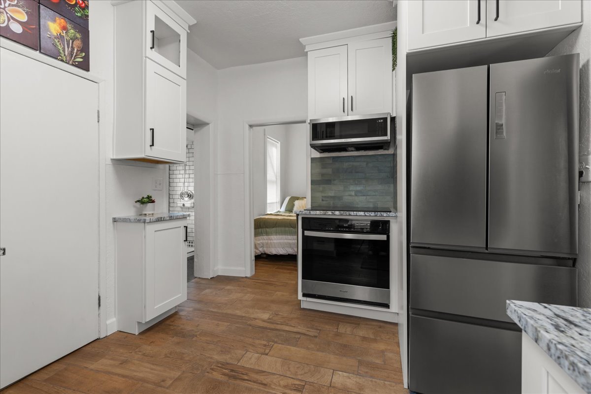 Kitchen with white cabinets, stainless steel appliances, light stone counters, dark wood-type flooring, and decorative backsplash