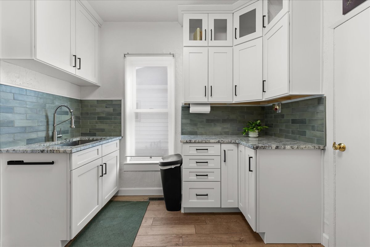 Kitchen with light stone counters, white cabinetry, and glass insert cabinets