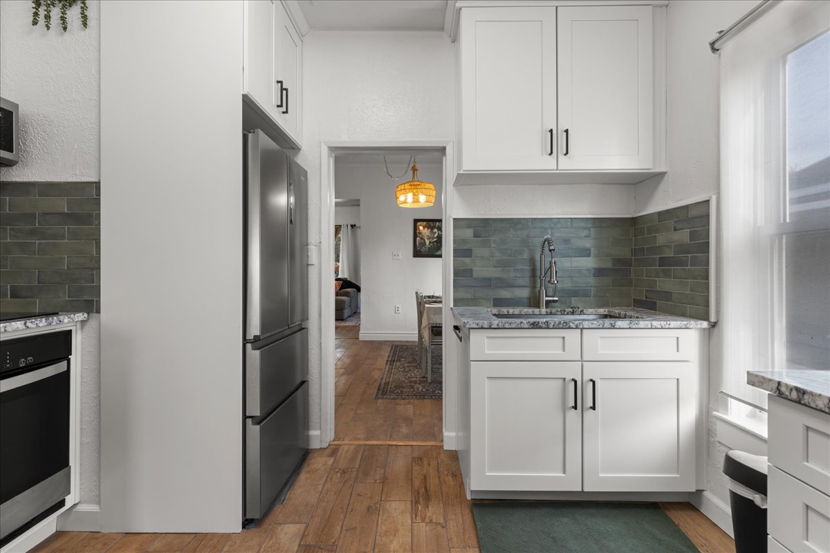 Kitchen with light stone countertops, decorative backsplash, stainless steel appliances, white cabinets, and a textured wall