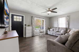 Living area with ceiling fan, dark wood-style flooring, and a textured ceiling