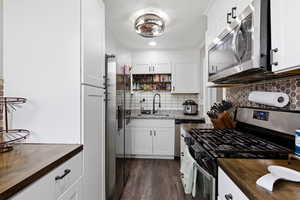 Kitchen with stainless steel appliances, open shelves, butcher block countertops, white cabinetry, and backsplash