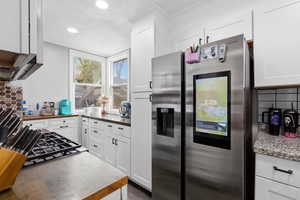 Kitchen with backsplash, stainless steel fridge, white cabinets, butcher block counters, and recessed lighting