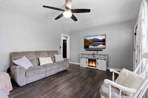Living area with wood finished floors, ceiling fan, a warm lit fireplace, and a textured ceiling