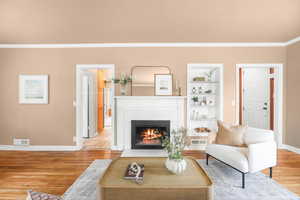 Living room with ornamental molding, light wood-type flooring, a fireplace with flush hearth, and built in features