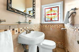 Half bathroom with a wainscoted wall and tile walls