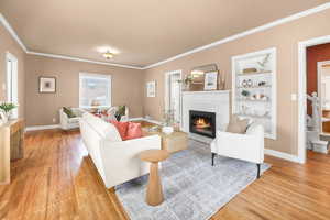 Living room with light wood-type flooring, a glass covered fireplace, ornamental molding, and built in features