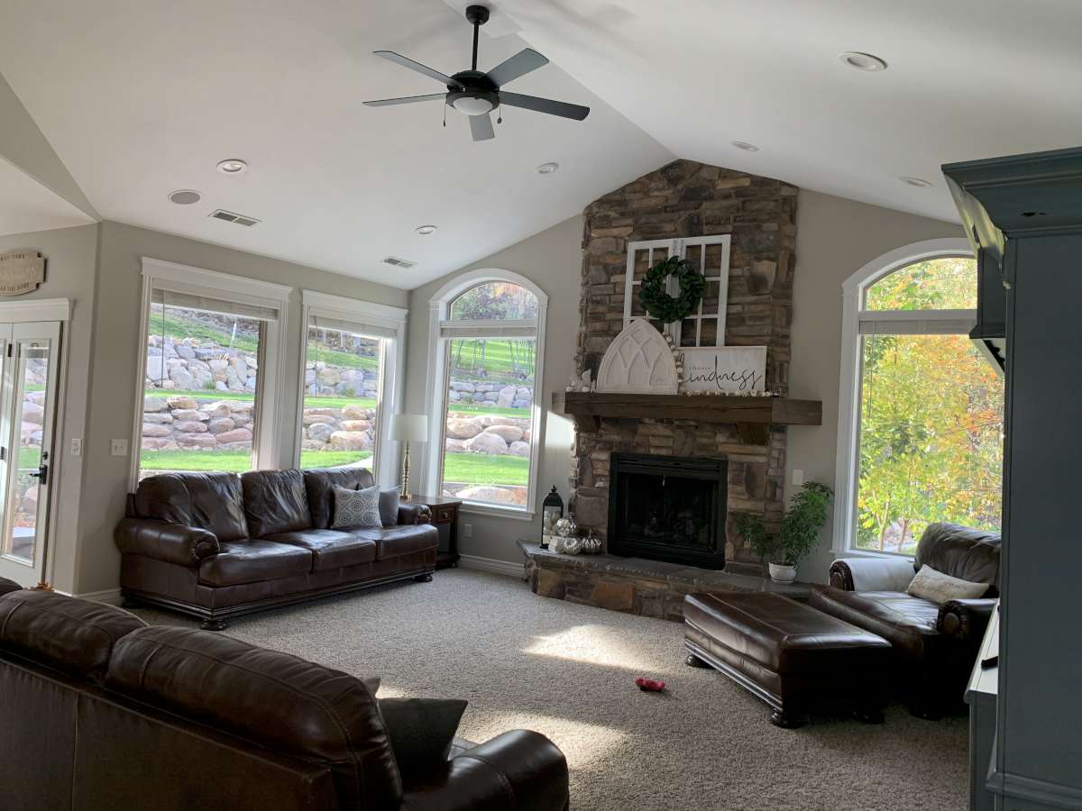 Living room with a ceiling fan, carpet flooring, plenty of natural light, and a stone fireplace
