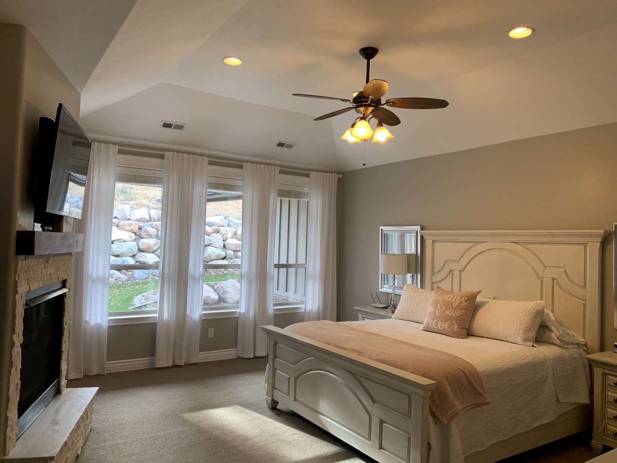 Bedroom with light colored carpet, recessed lighting, ceiling fan, lofted ceiling, and a fireplace with raised hearth