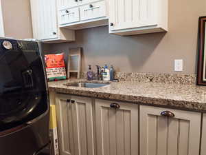 Kitchen with washer / clothes dryer, light stone counters, and white cabinets