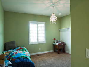 Carpeted bedroom with a chandelier and baseboards