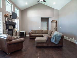 Living area featuring arched walkways, dark wood-style floors, ceiling fan, a stone fireplace, and a high ceiling
