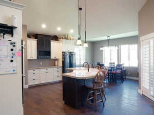 Dual tone kitchen featuring a breakfast bar, a kitchen island with sink, light stone counters, dual tone cabinets, and glass fronted cabinets