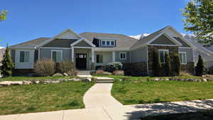 Craftsman-style home featuring stone siding, a front lawn, and a shingled roof