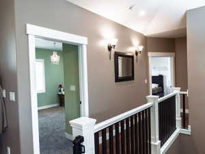 Corridor with carpet, an upstairs landing, suspended lighting, and lofted ceiling