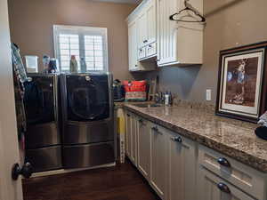 Laundry room with dark wood-style floors, washing machine and clothes dryer, and cabinet space