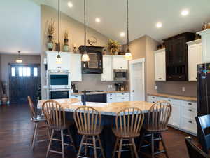 Kitchen with decorative light fixtures, stainless steel appliances, white cabinetry, and vaulted ceiling