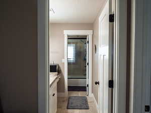 Bathroom with vanity, enclosed tub / shower combo, a textured ceiling, and light tile patterned floors