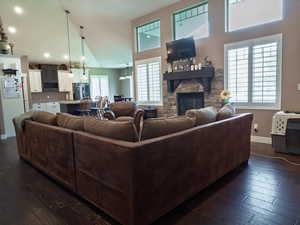 Living area with dark wood-style floors, a stone fireplace, lofted ceiling, and recessed lighting
