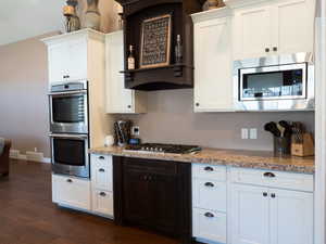 Kitchen with white cabinets, stainless steel appliances, extractor fan, dark wood-type flooring, and light stone counters