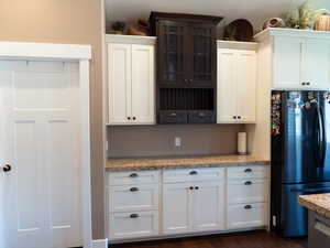 Kitchen with freestanding refrigerator, glass insert cabinets, white cabinetry, light stone countertops, and dark wood-style floors