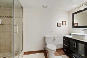 Full bath featuring vanity, a shower stall, dark tile patterned floors, and a textured ceiling