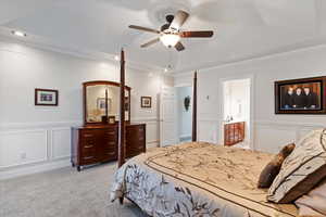 Bedroom with a decorative wall, a wainscoted wall, light carpet, a ceiling fan, and ornamental molding