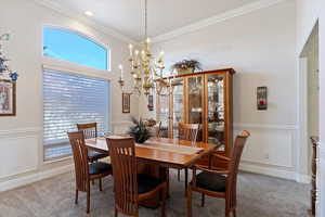 Carpeted dining area featuring a decorative wall, a wainscoted wall, crown molding, and a chandelier