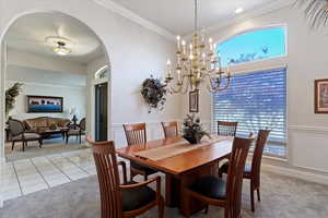 Dining space featuring light carpet, arched walkways, ornamental molding, a chandelier, and a decorative wall