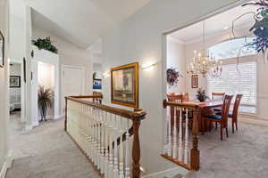 Hallway featuring light carpet, an upstairs landing, a chandelier, and ornamental molding