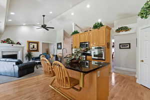 Kitchen featuring open floor plan, an island with sink, a kitchen bar, light wood-style floors, and lofted ceiling
