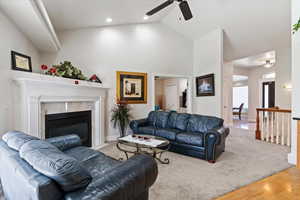 Living room featuring lofted ceiling, a ceiling fan, light carpet, light wood-style flooring, and a fireplace